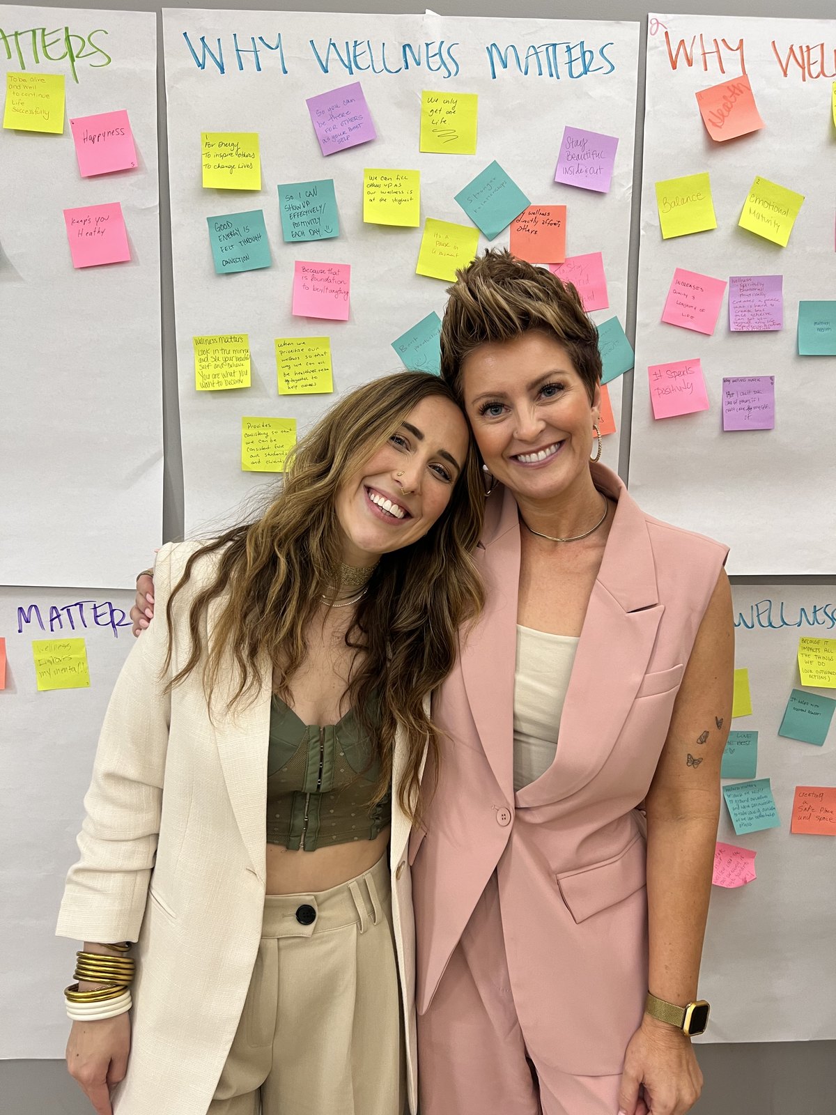 Elizabeth Faye with a school educator in front of the Why Wellness Matters wall