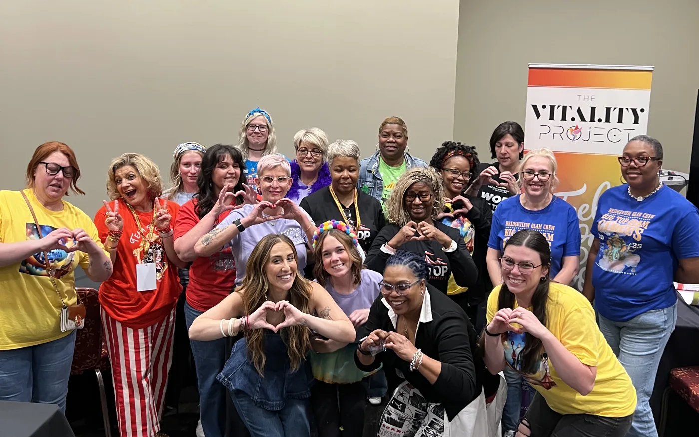 A school team making hearts with their hands in front of the Vitality Project banner
