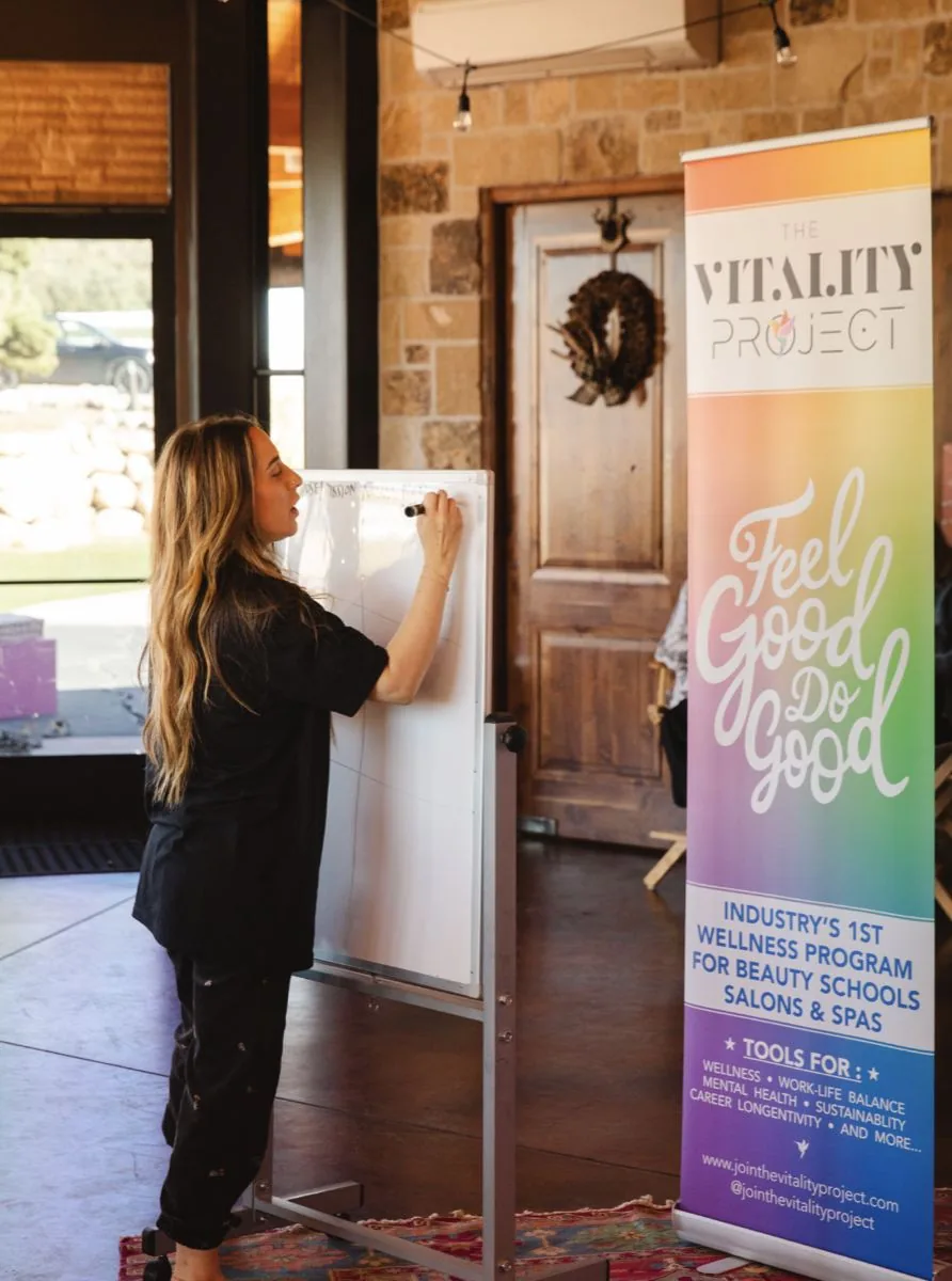 Elizabeth Faye teaching at a whiteboard beside the Vitality Project banner