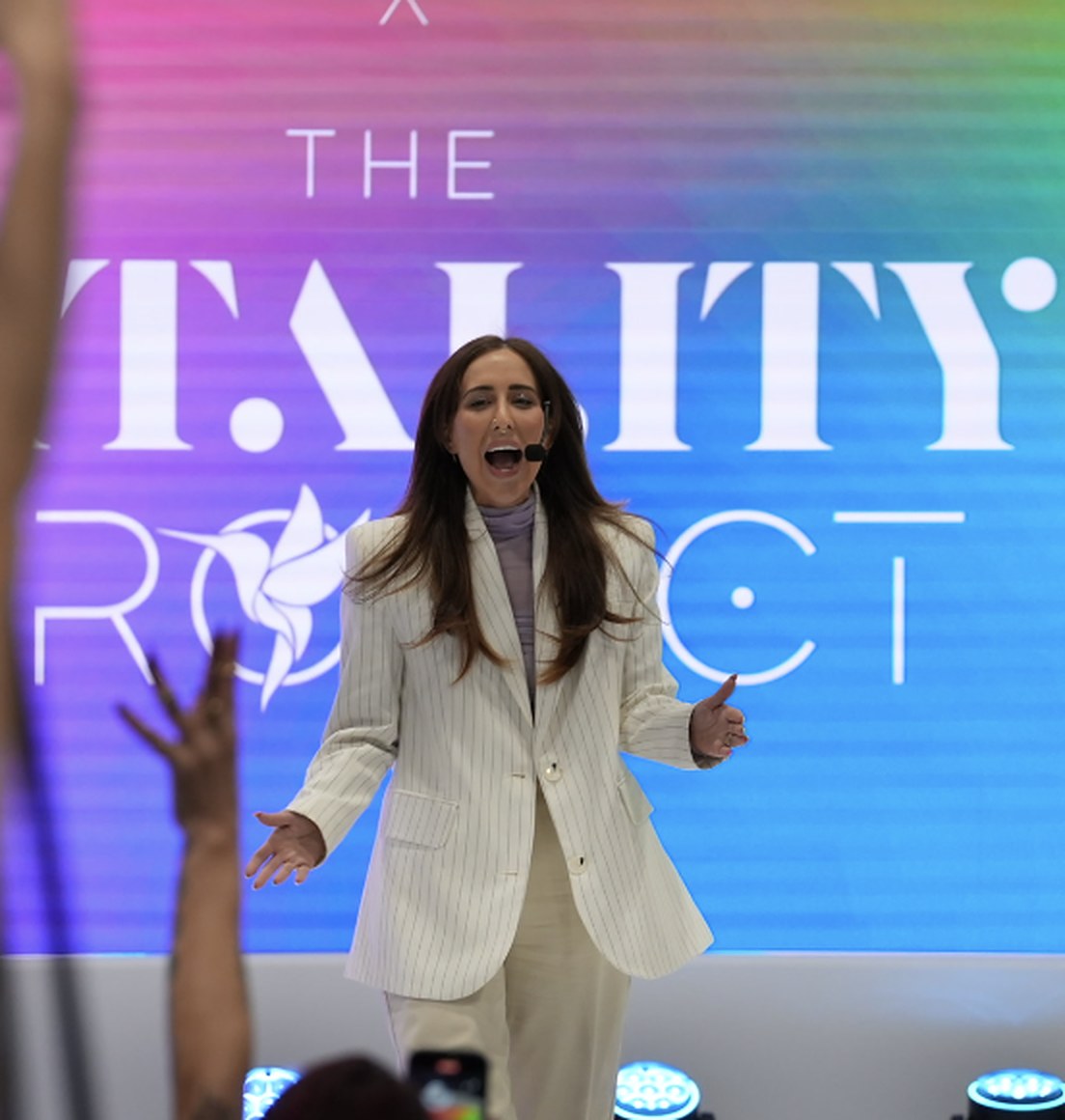 Elizabeth Faye on stage in front of the Vitality Project rainbow screen