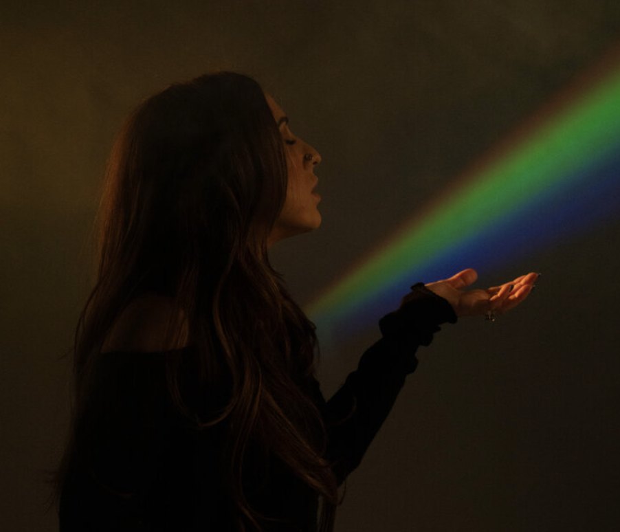 Elizabeth Faye holding a beam of rainbow light in a dark room